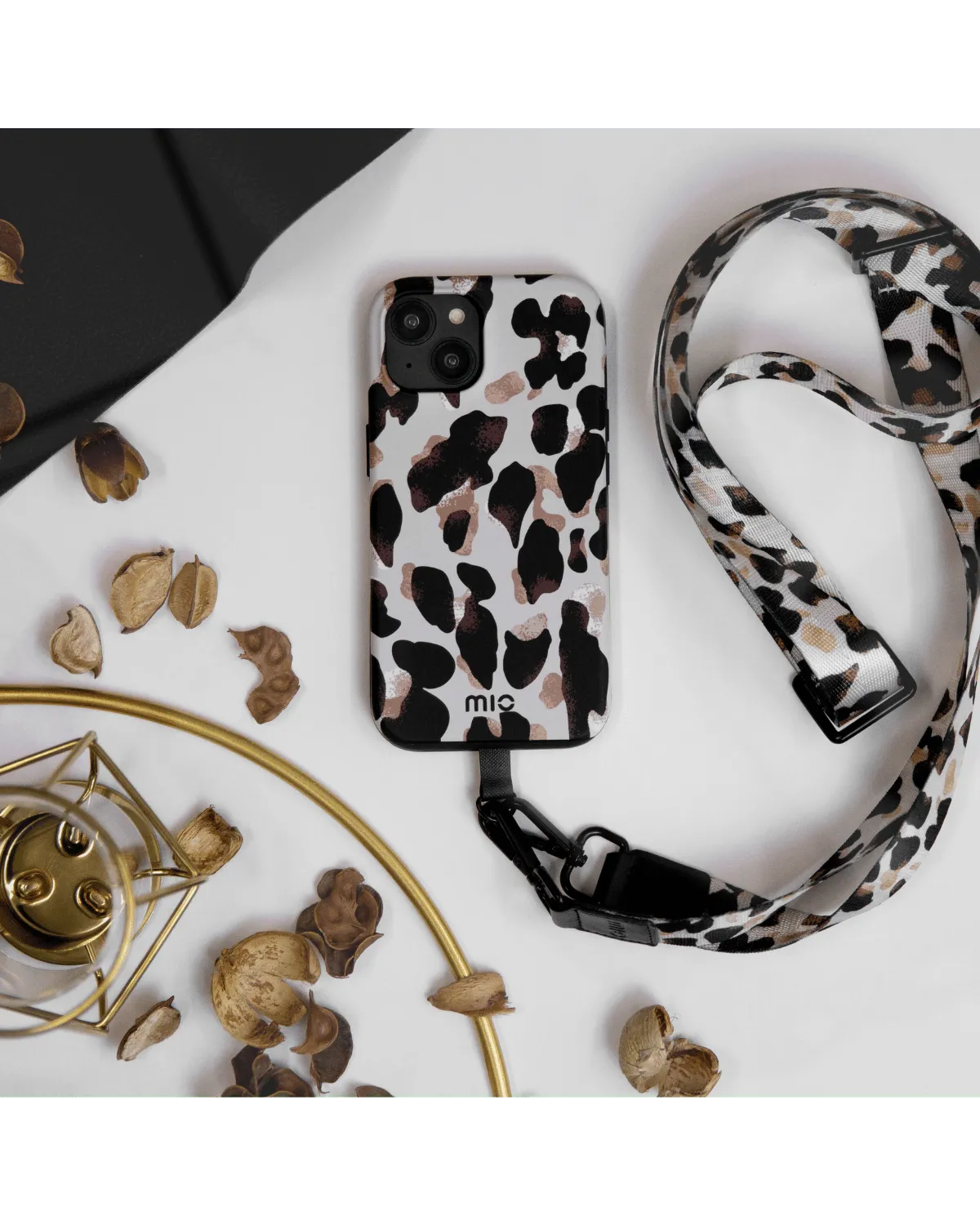 Mio Leopard hoesje liggend op tafel met bijpassend draagkoord en decoratie.