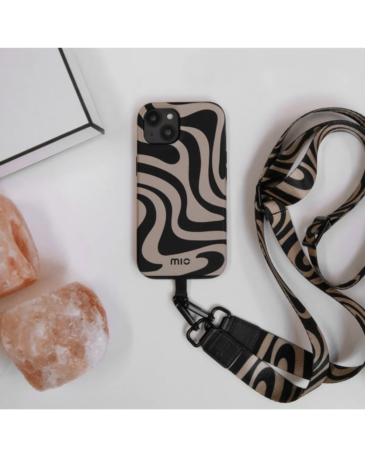 Mio Swirl telefoonhoes met bijpassend koord, liggend op tafel naast decoratieve objecten, stijlvol gepresenteerd.